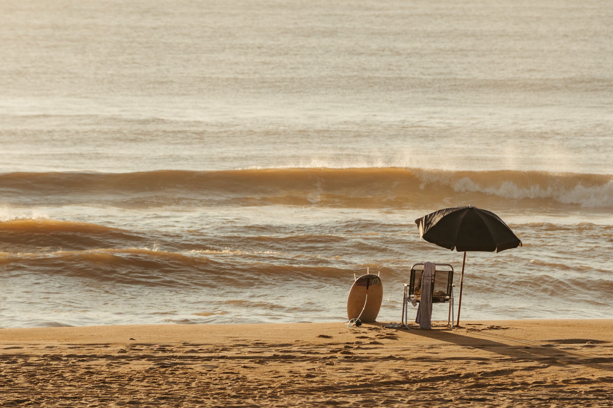 Une chaise de plage, un parasol et une planche de surf face à la mer, illustrant le slow travel et les vacances éthiques pour réduire le stress.