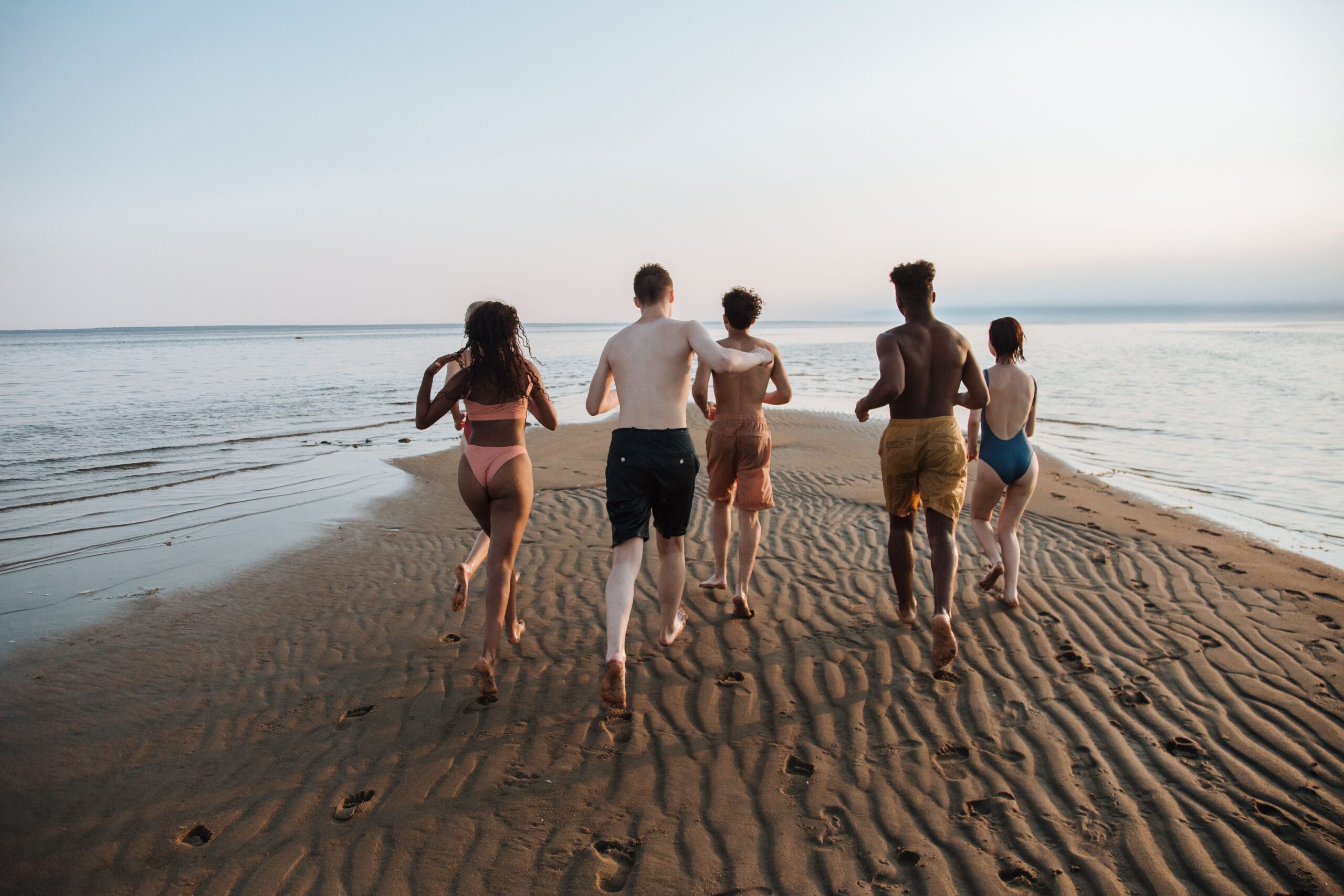 Un groupe d'amis courant sur la plage, illustrant les expériences authentiques en mode slow travel et tourisme durable.